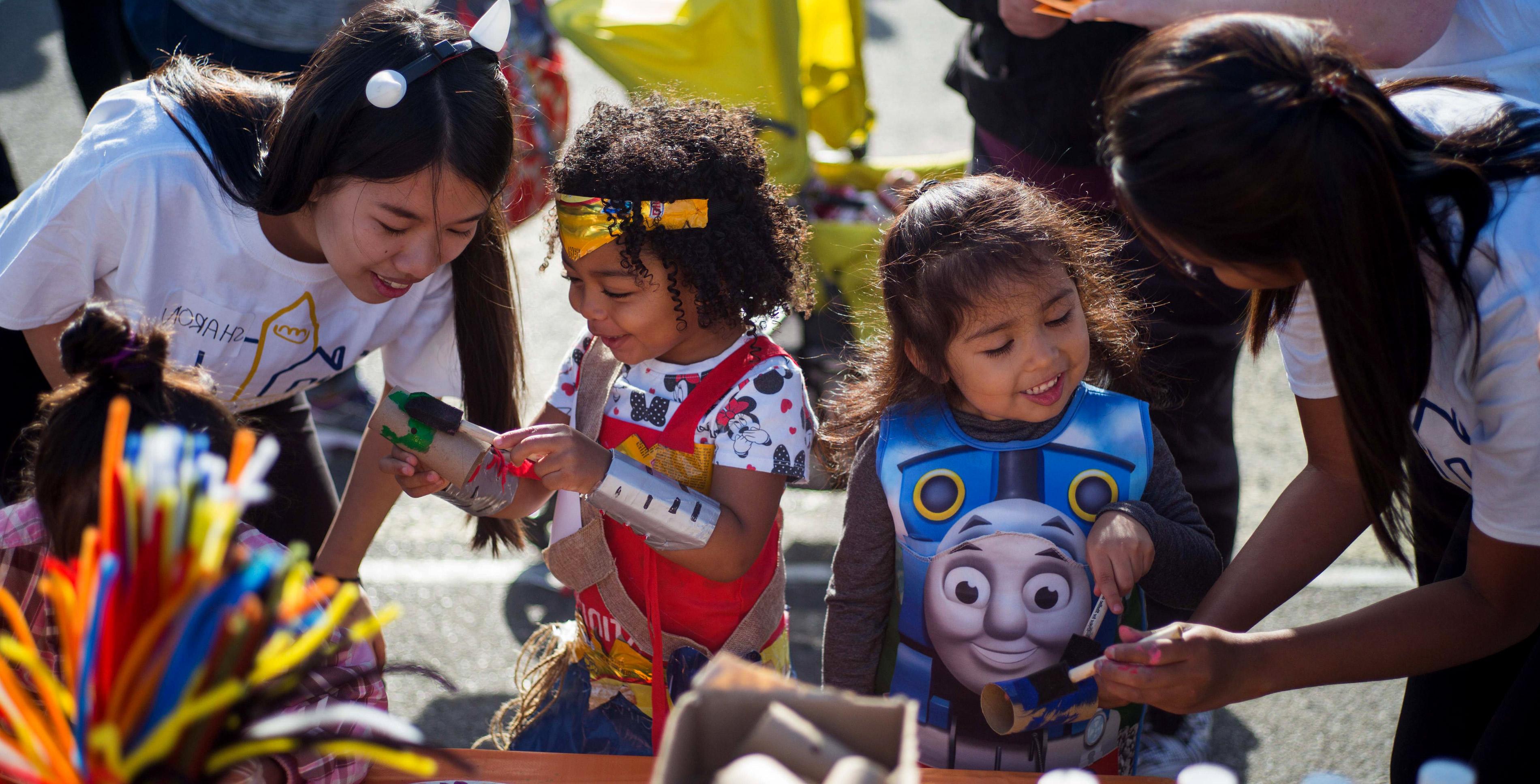 Student volunteers help two kids with arts and crafts during a halloween event.